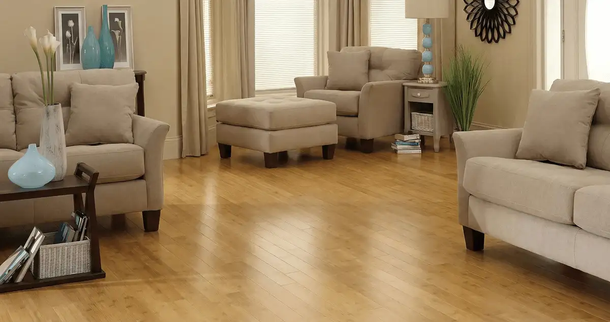 A living room with professionally installed bamboo flooring, beige sofas, a matching ottoman, a side table with a blue lamp, vases, framed pictures, and large windows with blinds and curtains in Spokane, WA