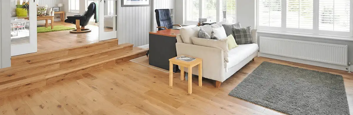 A modern living room with professionally installed laminate flooring, a beige sofa, a small side table, a gray rug, and large windows with white shutters in Spokane, WA